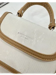 Détail de la texture en tissu rayé blanc et garniture en cuir marron du sac à bandoulière
