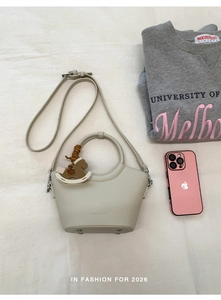 Detailansicht der beigefarbenen Beuteltasche mit Metallfüßen und Taschenanhänger