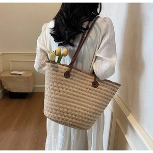 Close-up of woven straw tote bag with brown leather straps and striped texture