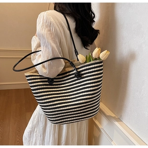 Close-up of woven black and white striped tote bag with fringe edge and leather straps