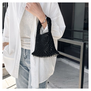 Detail of a black hand-woven mesh handbag showing hollow knot patterns on a wrist bag