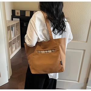 Dettaglio di una borsa tote in tela marrone con tasca a quadri e logo per il pendolare