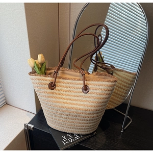 Close-up of woven tote bag with beige stripes, fringed edges and leather handles
