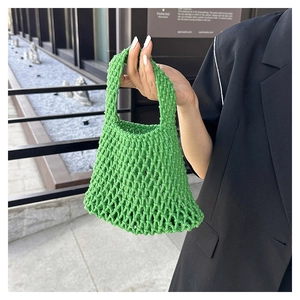 Close-up of grass green hollow woven tote bag held against a dark suit background