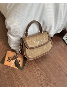 Détail d'un sac bandoulière marron avec rabat doré brossé et finitions métalliques argentées