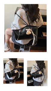 Detail of black glossy wrinkled tote bag with bear charm and white fringe tassel decor