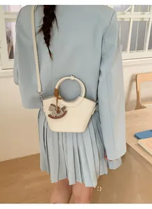 Detail einer cremefarbenen Beuteltasche mit rundem Griff und Holzpferd-Anhänger