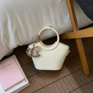 Detailansicht der cremefarbenen Eimer-Tasche aus Leder mit dekorativem Holzanhänger