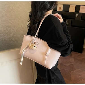 Detail of pink textured leather tote bag with a plush bear charm and knot strap design