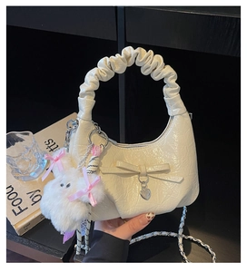 Détail du sac plissé crème avec nœud, pendentif en cœur et breloque lapin en peluche