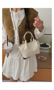 Detail view of cream white bucket bag featuring unique knotted handles and smooth leather
