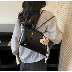 Detail view of glossy black tote bag with white lettering and cute bear charm