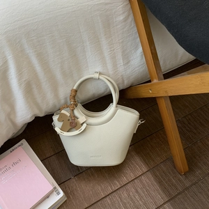 Detail der cremefarbenen Ledertasche mit Rundgriff und hölzernem Schaukelpferd-Anhänger