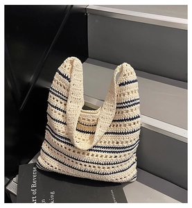 Detail of hollow woven shoulder bag with beige and navy stripes on grey stairs