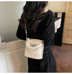 Detail view of beige textured bucket bag with woven handle on a model in urban setting