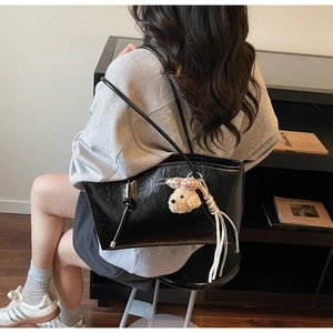 Detail of glossy black leather tote bag with a plush dog charm and white tassel on shoulder