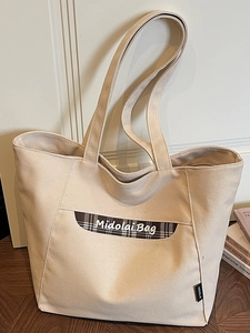 Sac fourre-tout en toile beige avec poche à carreaux marron sur un sol en bois naturel