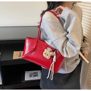 Detail of red tote bag featuring glossy crinkled texture and cute teddy bear charm