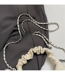 Gros plan détaillé d'un sac plissé crème avec bandoulière en chaîne et texture en cuir verni