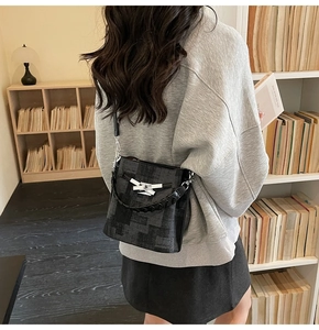 Close-up of black textured bucket bag with silver twist-lock and woven handle on model