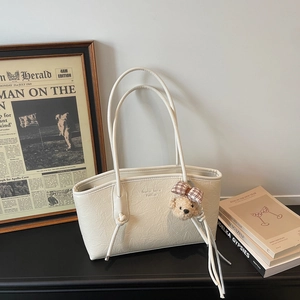 Close-up of beige tote bag with pleated texture, tassels and a cute bear charm