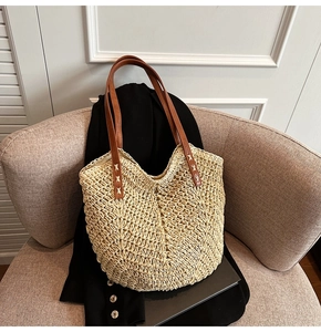Detail view of woven straw tote texture with brown leather straps on a beige sofa