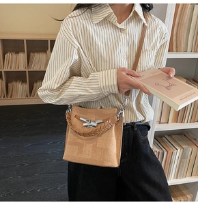Detail of camel shoulder bag with woven handle and metallic buckle in a library setting