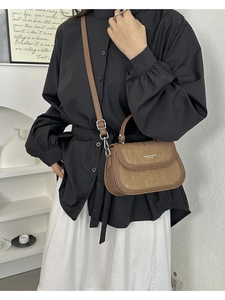Gros plan d'un sac bandoulière en cuir marron avec texture verticale et boucle en métal