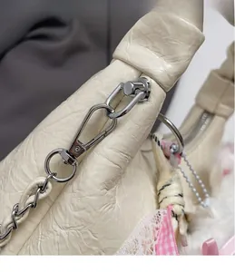 Gros plan du sac en cuir plissé crème avec détails argentés et nœud à carreaux rose