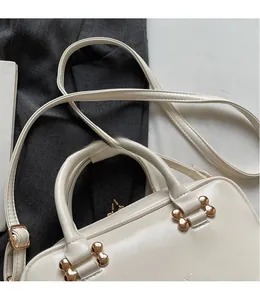 Detail view of cream white PU handbag with unique gold bone-shaped metal buckles and zipper