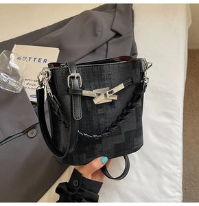 Close-up of black bucket bag with silver metal buckle and woven handle on stylish background