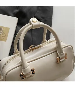 Close-up of cream Boston handbag featuring embossed letters and golden metal hardware
