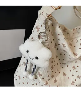 Close-up of a white cloud plush keychain with a smiley face on a corduroy tote bag