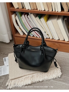 Detail of a vintage black leather bucket bag with knotted handle on a beige knit rug
