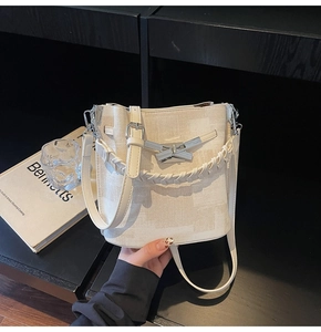 Detail view of cream woven bucket bag with metallic cross lock and dual strap system