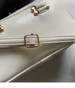 Detailed macro view of the matte white leather texture and gold metal buckle on handbag