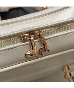 Detail shot of golden dachshund-shaped zipper slider on beige leather bowling handbag