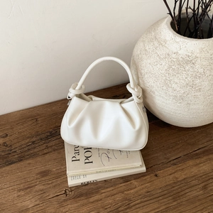 Dettaglio borsa a nuvola plissettata bianca su tavolo in legno con decori eleganti