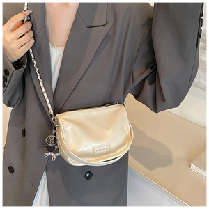 Close-up of beige glossy small square bag featuring metal rabbit charm and chain strap