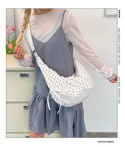 Detail view of large white canvas crossbody bag with black polka dots and side drawstring bow