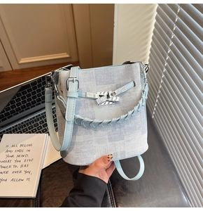 Detail of light blue denim bucket bag with silver turn-lock and woven handle on desk