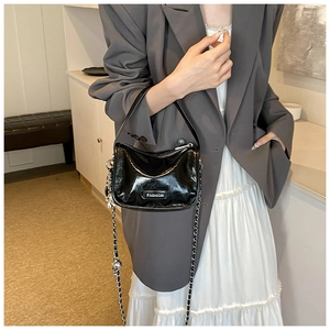 Detail of a black glossy patent leather mini bag featuring a silver fashion label and chain