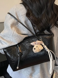Chic black glossy tote bag with dog plush charm shown on model in a casual outfit