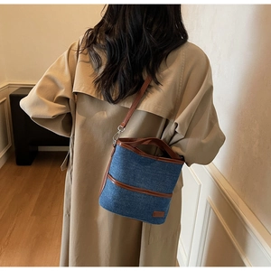 Detail der blauen Denim-Beuteltasche mit braunem Lederbesatz und beigem Trenchcoat