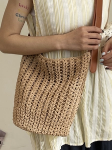 Minimalist hand-woven straw tote bag with brown leather shoulder strap shown on a model