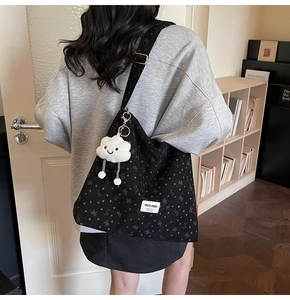 Detail of black corduroy tote bag with heart patterns and soft cloud charm accessory
