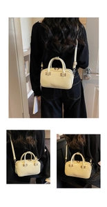 Detail view of a cream Boston bag with round handles and long strap in a home setting