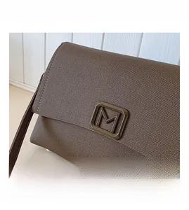 Detailed close-up of brown textured fabric bag featuring a metallic M-shaped hardware buckle