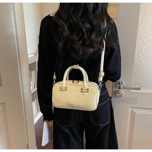 Cream white leather handbag with gold zipper and adjustable strap shown on shoulder