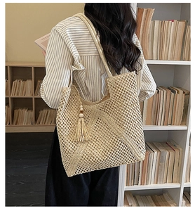 Detailed close-up of woven hollow mesh pattern and wood bead tassel on beige straw tote bag